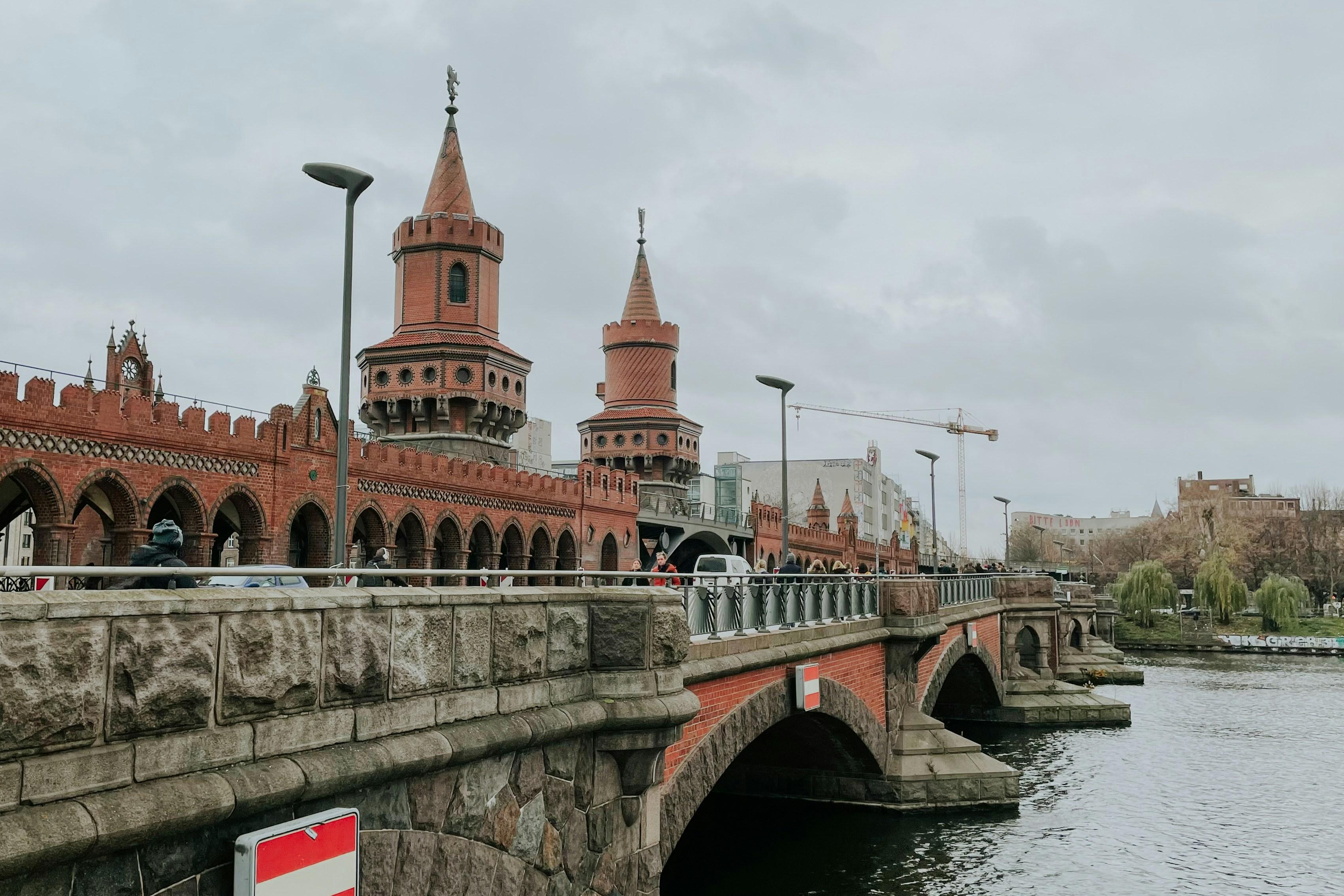 Most w Berlinie, pochmurna pogoda, w oddali widać zabudowania i dźwig przemysłowy.